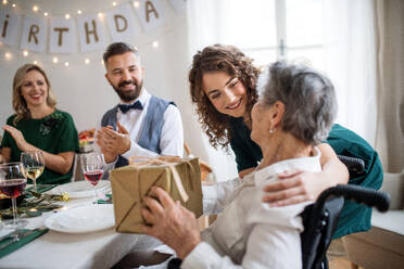 Eine ältere Großmutter im Rollstuhl feiert ihren Geburtstag mit ihrer Familie und erhält ein Geschenkpaket, ein Partykonzept. - HPIF17461