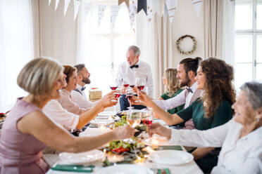 Eine große Familie sitzt an einem Tisch auf einer Indoor-Geburtstagsfeier und stößt mit Rotwein an. - HPIF17464