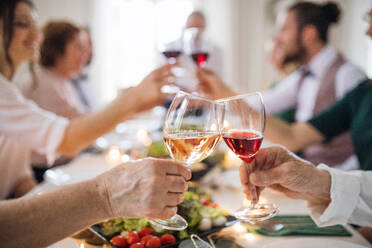 Eine große Familie oder Freunde, die auf einer Indoor-Geburtstagsfeier an einem Tisch sitzen und mit Gläsern anstoßen. - HPIF17465