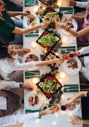 Draufsicht auf eine große Familie, die auf einer Indoor-Geburtstagsfeier an einem Tisch sitzt und mit Gläsern anstößt, ein Mittelteil. - HPIF17495