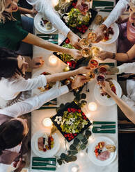 Ein Mittelteil einer großen Familie oder von Freunden, die auf einer Indoor-Geburtstagsparty an einem Tisch sitzen und mit Gläsern anstoßen, Ansicht von oben. - HPIF17496