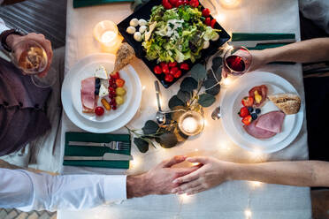 A top view of a couple in love sitting at a table on a indoor family party, holding glasses with wine. - HPIF17497