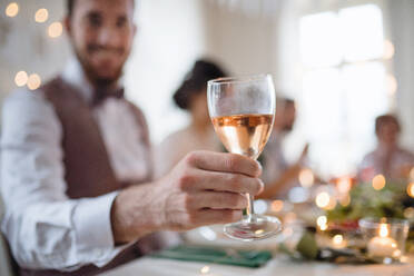 Nahaufnahme einer männlichen Hand in einem für eine Party eingerichteten Raum, die ein Glas Weißwein hält. - HPIF17498