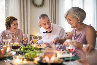 Fröhliche Senioren, die auf einer Indoor-Familiengeburtstagsfeier am Tisch sitzen und essen. - HPIF17503