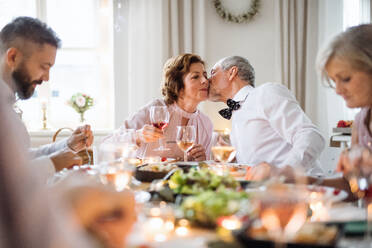 A senior couple sitting at a table on a indoor birthday party, kissing when eating. - HPIF17504