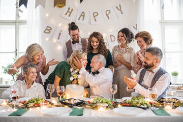 Ein älterer Mann mit einer Mehrgenerationenfamilie und einer Torte feiert seinen Geburtstag auf einer Indoor-Party. - HPIF17506