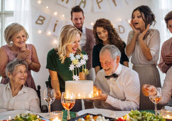 Ein älterer Mann mit einer Mehrgenerationenfamilie und einer Torte feiert seinen Geburtstag auf einer Indoor-Party. - HPIF17507