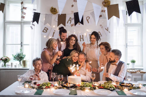 Ein älterer Mann mit einer Mehrgenerationenfamilie und einer Torte feiert seinen Geburtstag auf einer Indoor-Party. - HPIF17508