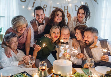 Ein älterer Mann mit einer Mehrgenerationenfamilie und einer Torte feiert seinen Geburtstag auf einer Indoor-Party. - HPIF17509