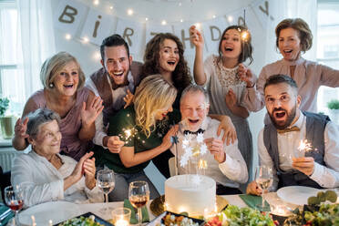 Ein älterer Mann mit einer Mehrgenerationenfamilie und einer Torte feiert seinen Geburtstag auf einer Indoor-Party. - HPIF17510