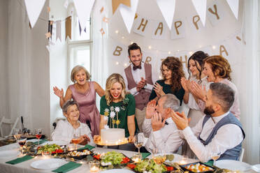 Ein älterer Mann mit einer Mehrgenerationenfamilie und einer Torte feiert seinen Geburtstag auf einer Indoor-Party. - HPIF17512
