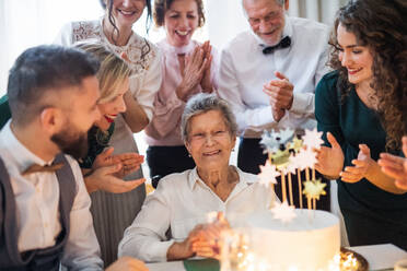 Eine ältere Frau mit einer Mehrgenerationenfamilie und einer Torte feiert ihren Geburtstag auf einer Indoor-Party. - HPIF17514