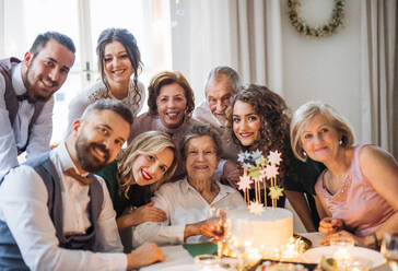 Eine ältere Frau mit einer Mehrgenerationenfamilie und einer Torte feiert ihren Geburtstag auf einer Indoor-Party. - HPIF17515