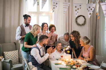 Eine ältere Frau mit einer Mehrgenerationenfamilie und einer Torte feiert ihren Geburtstag auf einer Indoor-Party. - HPIF17518