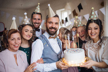 Ein Porträt einer Mehrgenerationenfamilie mit Kuchen und Partyhüten auf einer Indoor-Geburtstagsfeier. - HPIF17519