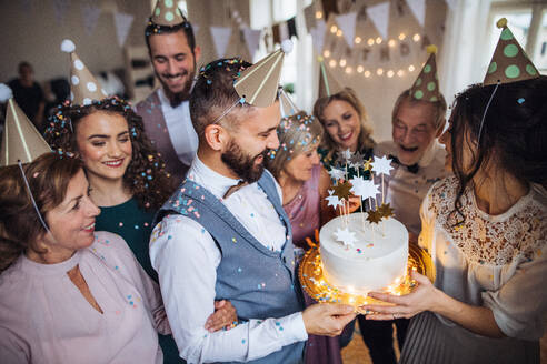 Ein Porträt einer Mehrgenerationenfamilie mit Kuchen und Partyhüten auf einer Indoor-Geburtstagsfeier. - HPIF17520