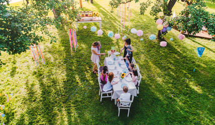 Blick von oben auf kleine Kinder, die auf einer Gartenparty im Sommer draußen am Tisch sitzen. - HPIF17557