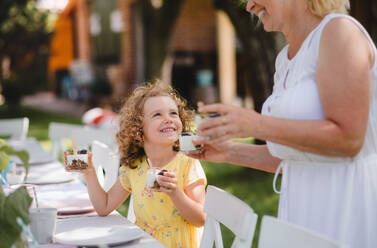 Glückliches kleines Mädchen mit unkenntlicher Großmutter im Freien auf Gartenparty im Sommer, Essen. - HPIF17571