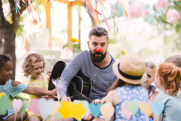 Ein Mann mit kleinen Kindern sitzt im Sommer draußen im Garten auf dem Boden und spielt Gitarre. - HPIF17587