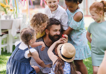 A man with small children sitting on ground outdoors in garden in summer, playing. - HPIF17594