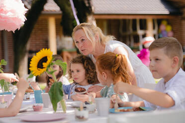 Group of small children sitting at the table outdoors on garden party, eating. - HPIF17606