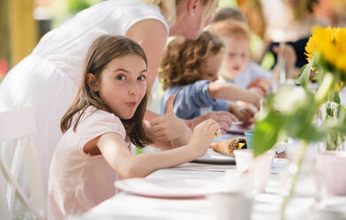 Group of small children sitting at the table outdoors on garden party in summer, eating. - HPIF17608