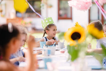 Group of small children sitting at the table outdoors on garden party in summer, eating. - HPIF17609