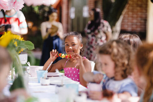 Eine Gruppe von kleinen Kindern sitzt am Tisch im Freien auf einer Gartenparty und isst. - HPIF17611