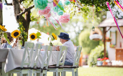 Ein kleiner Junge sitzt am Tisch im Freien auf einer Gartenparty im Sommer und isst. - HPIF17614