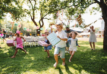 Kleine Kinder laufen mit Geschenk im Freien im Garten auf Geburtstagsfeier, spielen. - HPIF17620