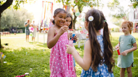 Small children standing outdoors in garden in summer, playing. A celebration concept. - HPIF17625