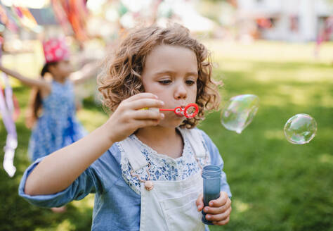 Small girl blowing bubbles outdoors in garden in summer, birthday celebration concept. - HPIF17626