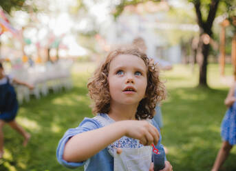 Small girl blowing bubbles outdoors in garden in summer, birthday celebration concept. - HPIF17627