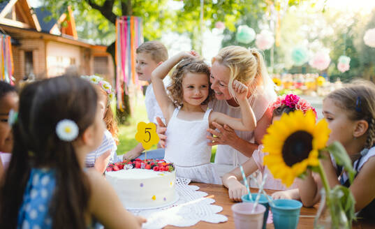 Eine Gruppe von kleinen Kindern sitzt am Tisch im Freien auf einer Gartenparty. - HPIF17642