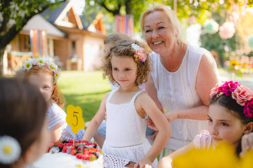 Eine Gruppe von kleinen Kindern sitzt am Tisch im Freien auf einer Gartenparty. - HPIF17643