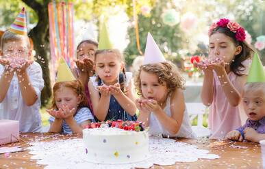 Ein Porträt von Kindern mit Kuchen, die auf einer Geburtstagsfeier im Garten im Sommer um einen Tisch herum stehen. - HPIF17648