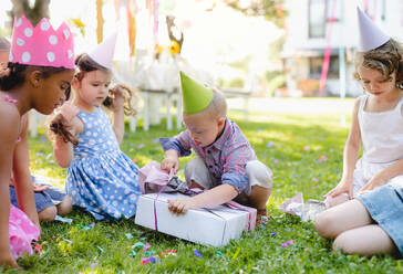 Down-Syndrom-Kind mit Freunden auf Geburtstagsparty im Freien im Garten, Öffnen von Geschenken. - HPIF17652