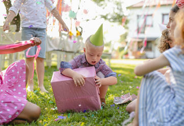 Down-Syndrom-Kind mit Freunden auf Geburtstagsparty im Freien im Garten, Öffnen von Geschenken. - HPIF17653