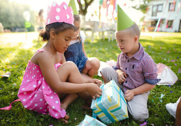 Down-Syndrom-Kind mit Freunden auf Geburtstagsparty im Freien im Garten, Öffnen von Geschenken. - HPIF17654