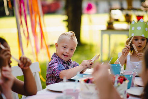 Down-Syndrom-Kind mit Freunden auf Geburtstagsfeier im Freien im Garten im Sommer. - HPIF17658
