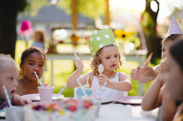 Eine Gruppe von kleinen Kindern sitzt am Tisch im Freien auf einer Gartenparty und isst. - HPIF17660