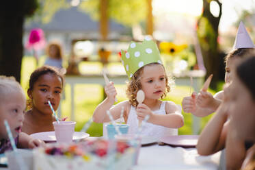 Group of small children sitting at the table outdoors on garden party, eating. - HPIF17660