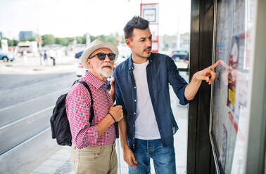 Ein junger Mann und ein blinder Senior mit weißem Stock stehen an einer Bushaltestelle in der Stadt und lesen den Fahrplan. - HPIF17714