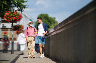 A young man and blind senior with white cane walking on pavement in city, talking. - HPIF17728