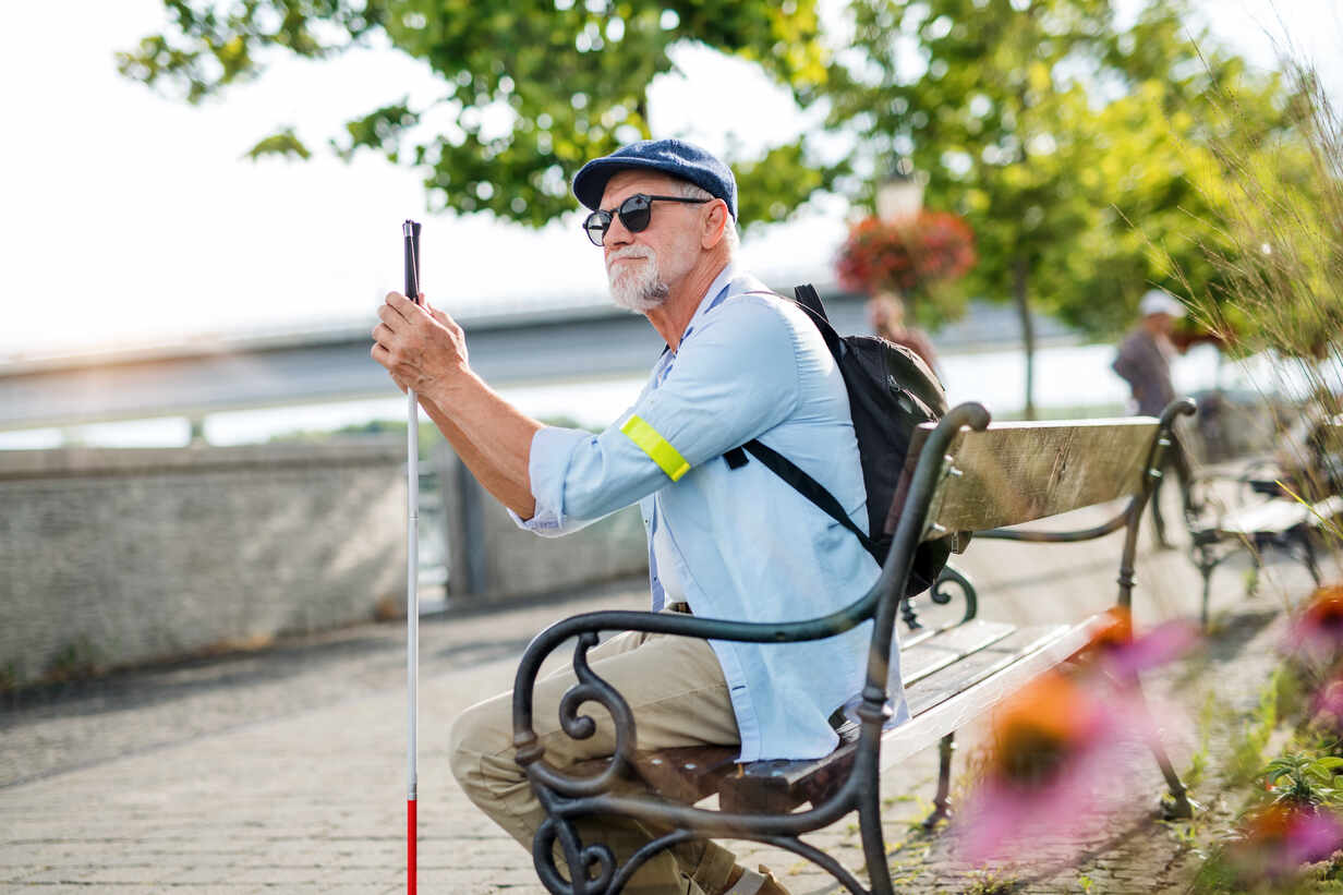 A senior blind man with white cane getting on public transport in city.  stock photo