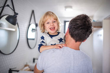 Mature father carrying small son indoors in bathroom, having fun. - HPIF17746