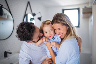 Eine junge Familie mit kleiner Tochter im Badezimmer, die sich umarmen. - HPIF17748