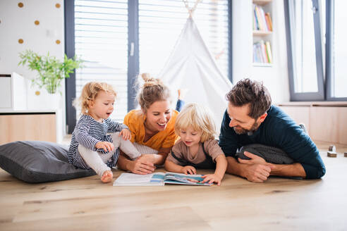 Vorderansicht einer jungen Familie mit zwei kleinen Kindern, die im Schlafzimmer ein Buch lesen. - HPIF17766