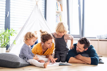 Front view of young family with two small children indoors in bedroom reading a book. - HPIF17767