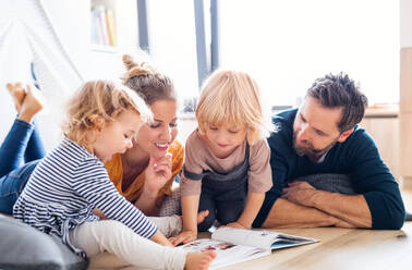 Vorderansicht einer jungen Familie mit zwei kleinen Kindern, die im Schlafzimmer ein Buch lesen. - HPIF17768